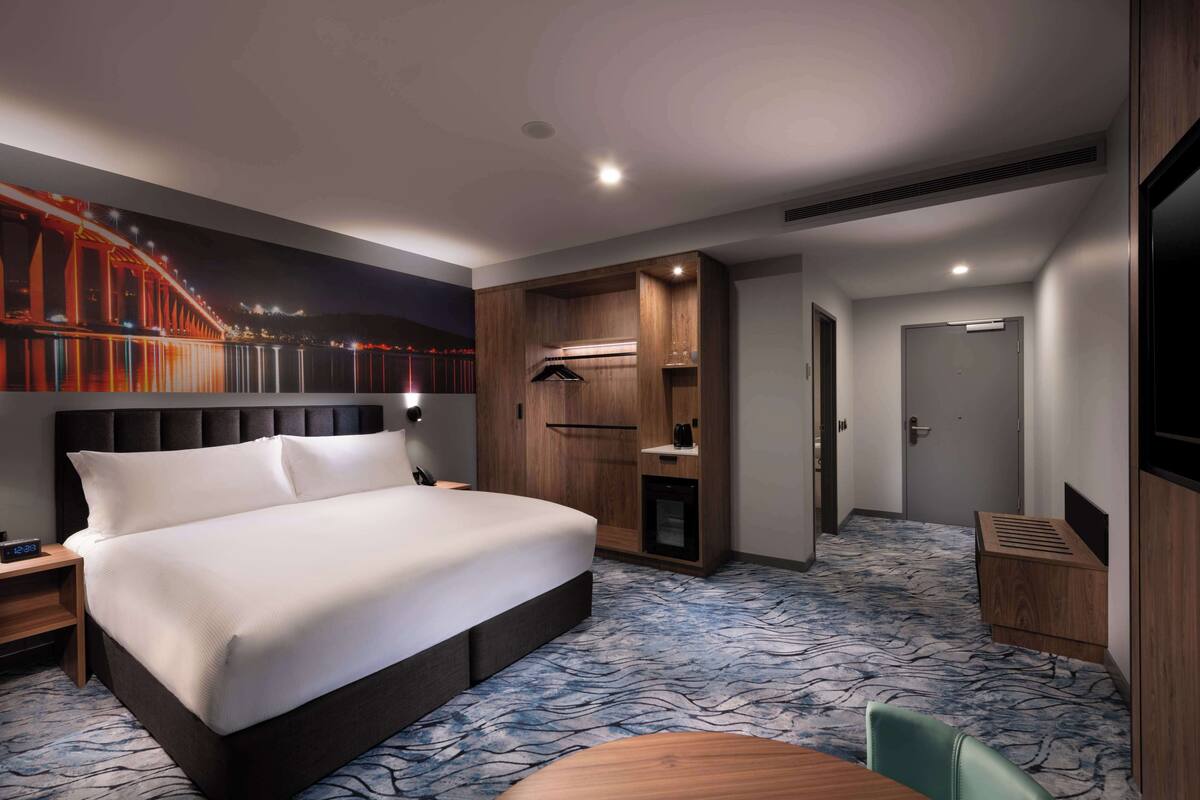 A hotel room with a large bed, a wardrobe, a desk, and a television.
