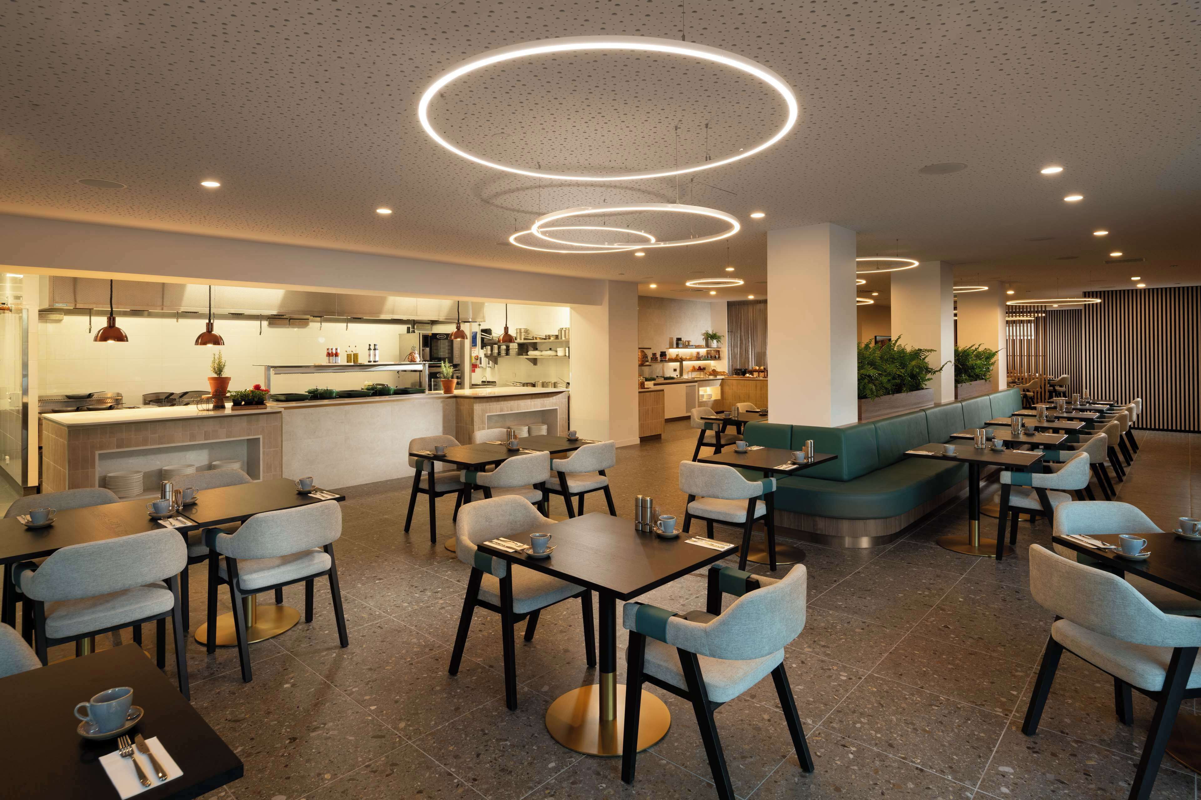 Un restaurante moderno con varias zonas de comedor, incluyendo un bar y asientos con mesas y sillas redondas.
