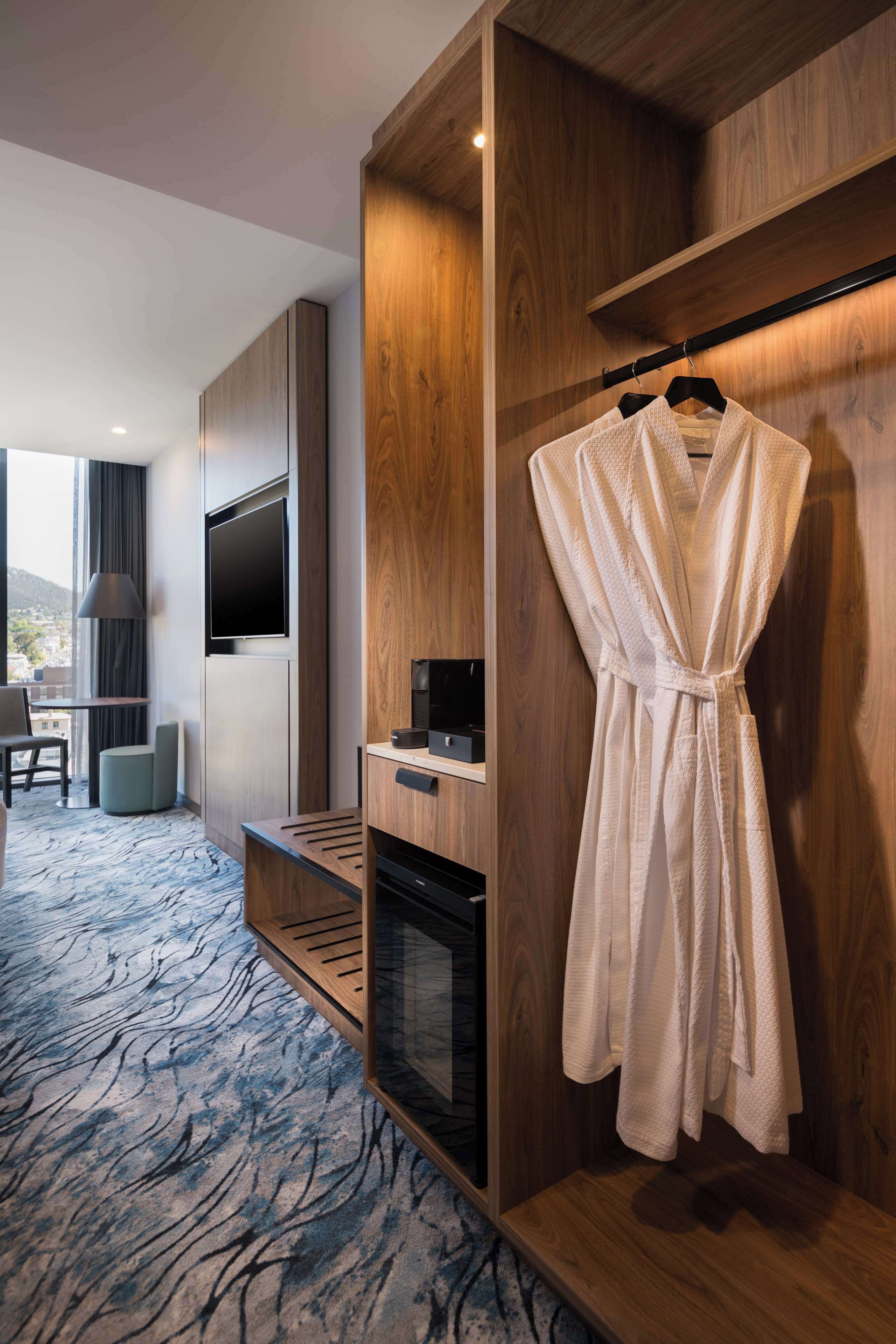 Une chambre d’hôtel avec une armoire en bois, un peignoir suspendu, un téléviseur à écran plat, un bureau et une vue sur l’extérieur.
