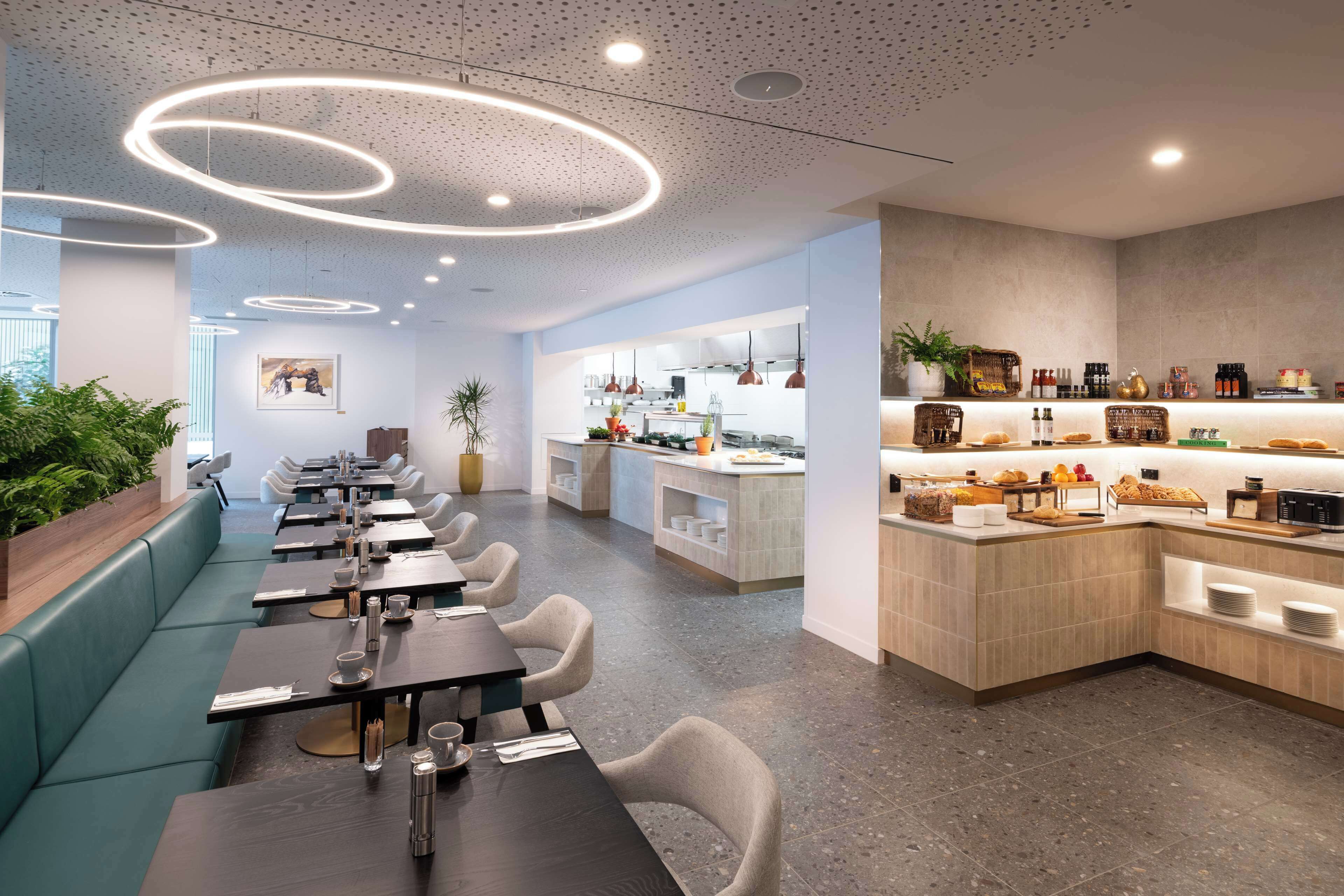 A modern restaurant with a long counter, seating area, and a kitchen visible in the background.