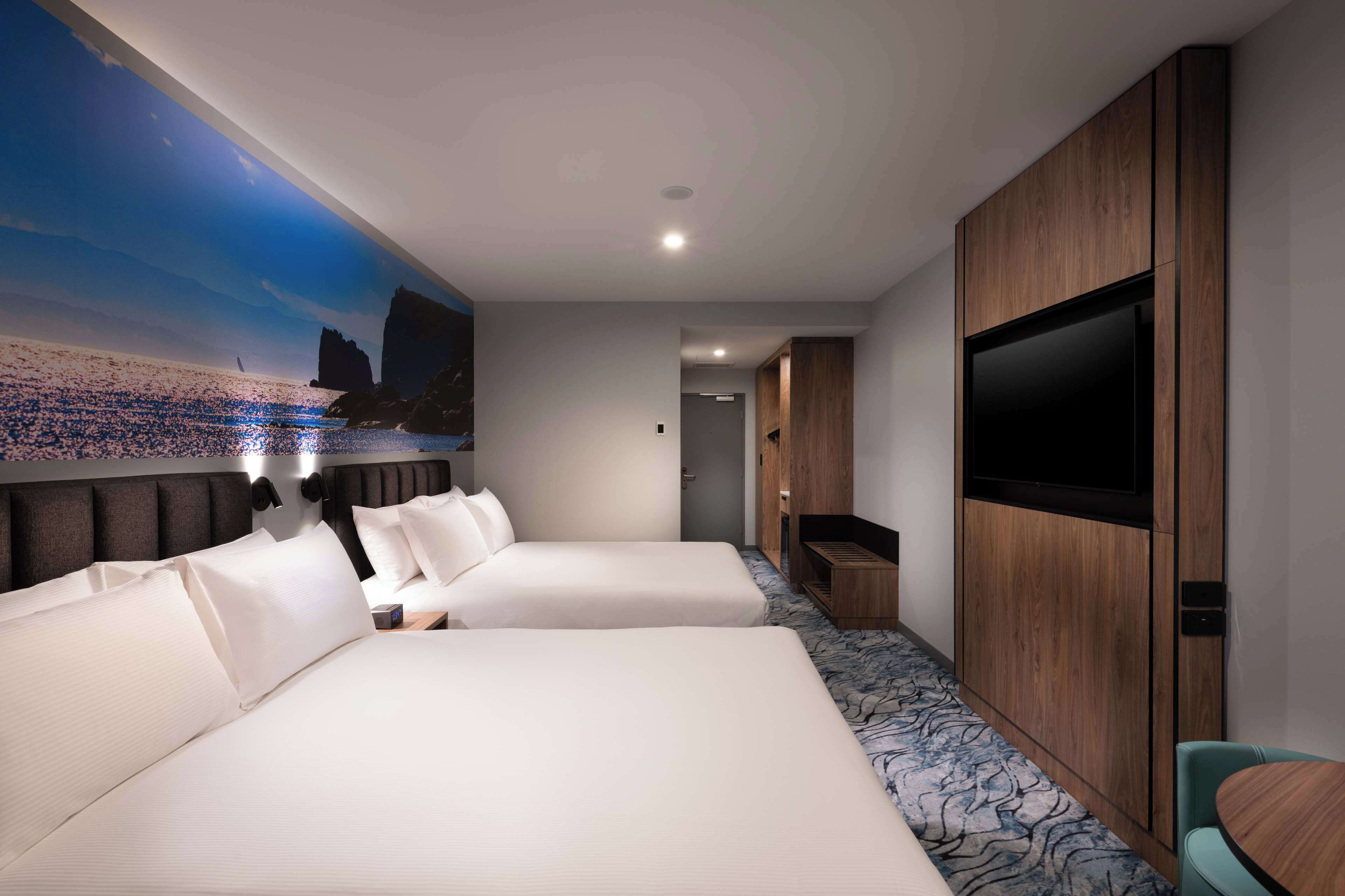 Une chambre d’hôtel avec deux lits, une grande télévision et une fresque représentant une scène de plage.