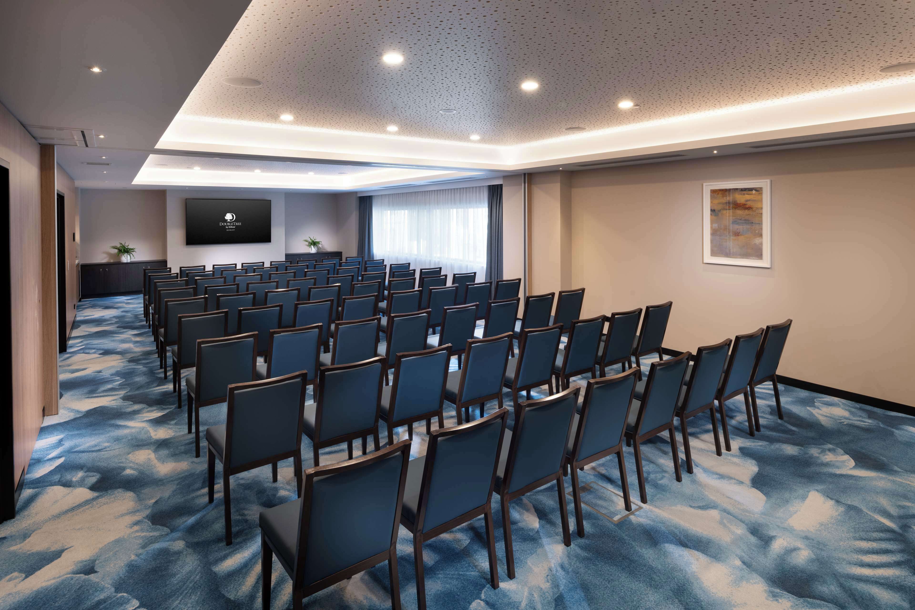 Una sala conferenze con file di sedie, un grande schermo e pavimento rivestito di moquette.