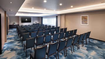 Una sala conferenze con file di sedie, un grande schermo e pavimento rivestito di moquette.