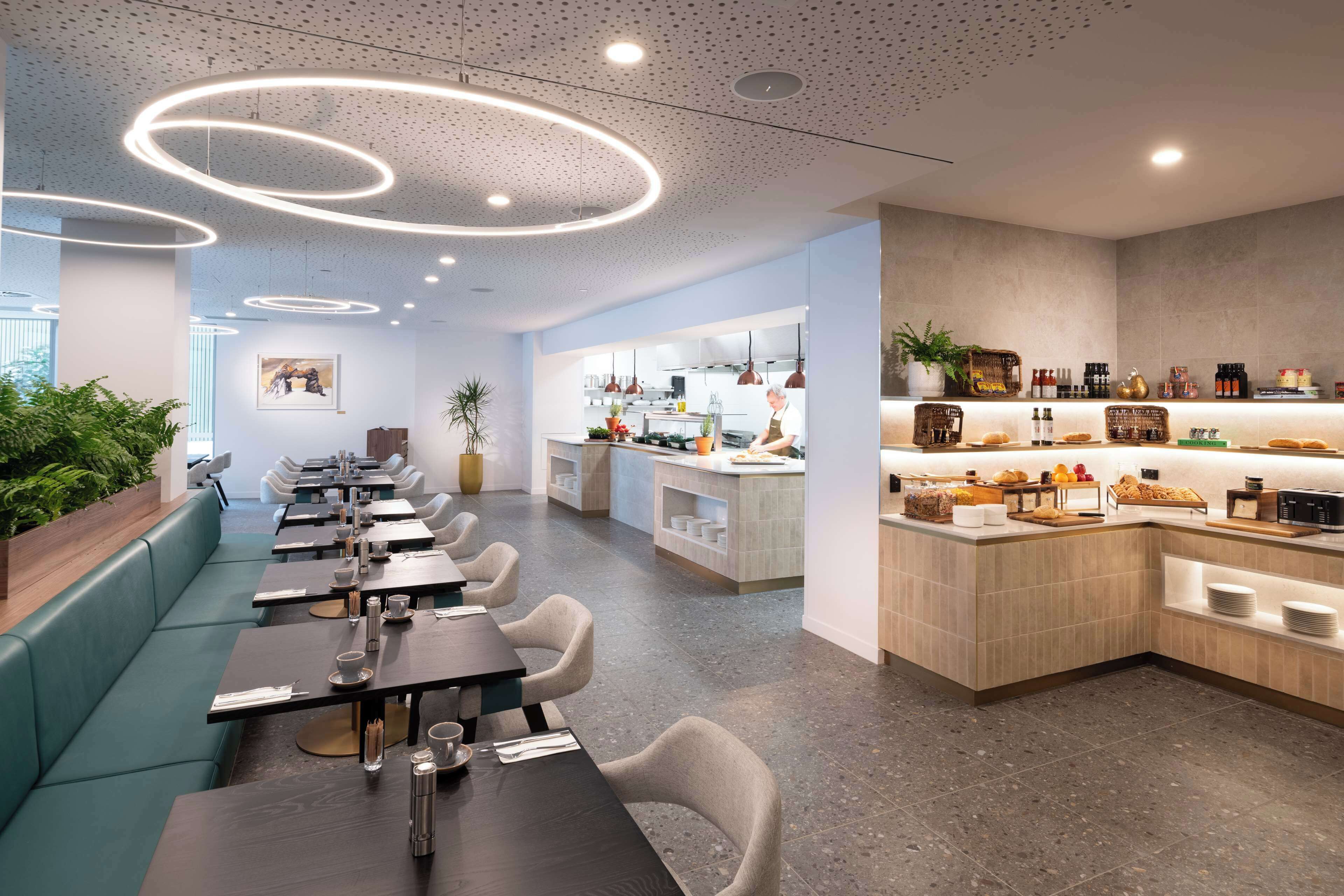 A modern restaurant with a long counter, seating area, and a kitchen visible in the background.