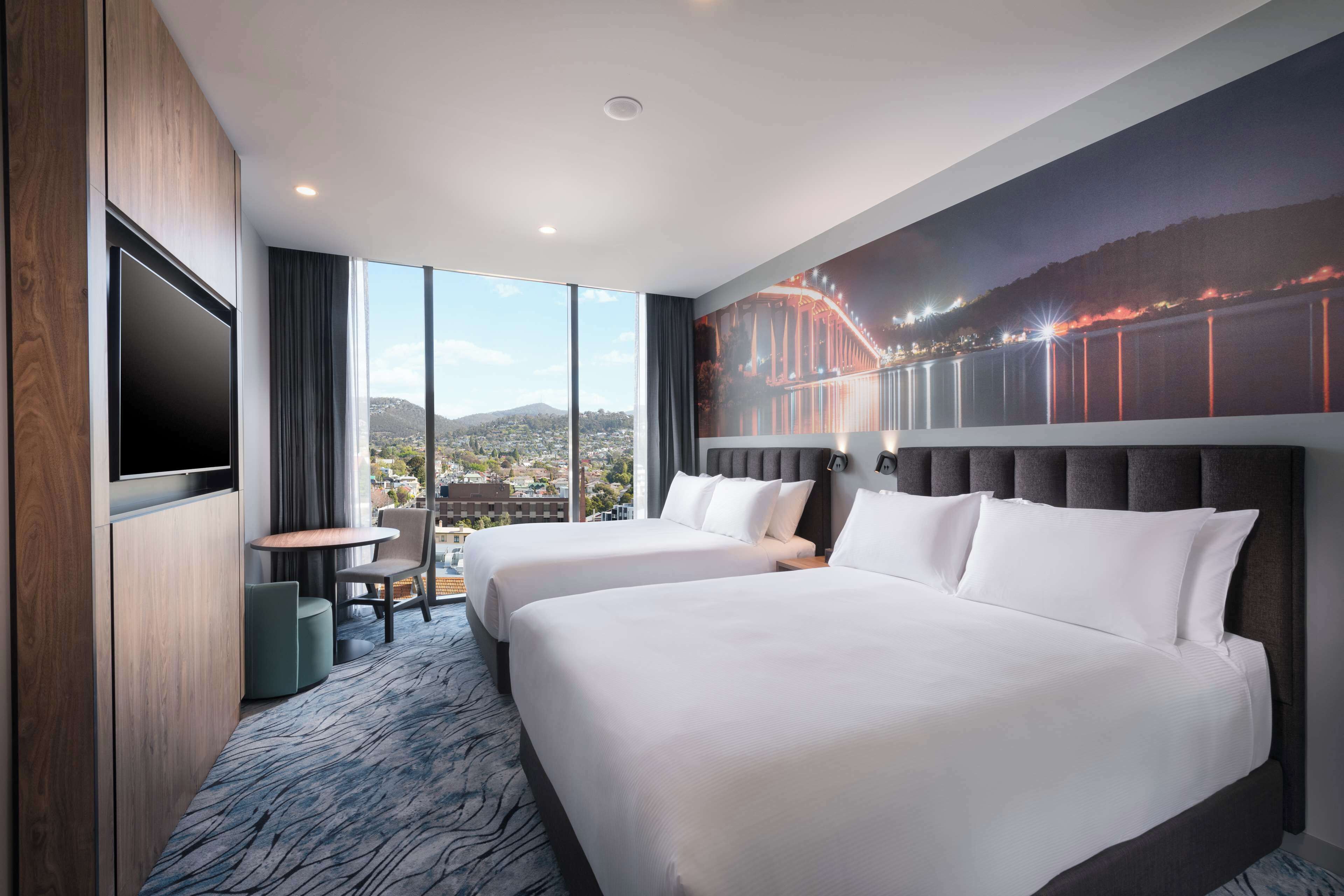 A hotel room with two beds, a TV, a small table, and a chair.