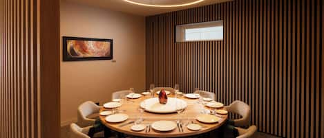 A round dining table with eight chairs, a central vase, and a window in the background.