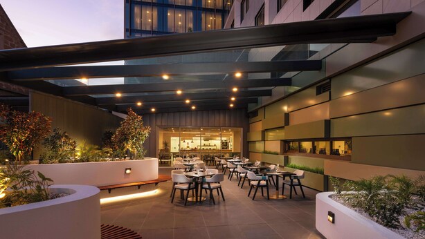 An outdoor dining area with tables and chairs, surrounded by planters and a modern building facade. - Doubletree By Hilton Hobart (Hobart)
