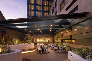 An outdoor dining area with tables and chairs, surrounded by planters and a modern building facade. - Doubletree By Hilton Hobart (Hobart)
