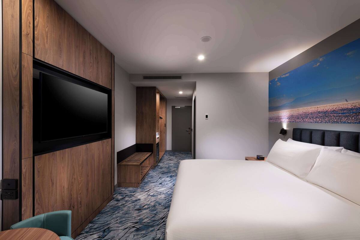 A hotel room with a large bed, a TV mounted on the wall, a wooden wardrobe, and a mural of a beach scene.