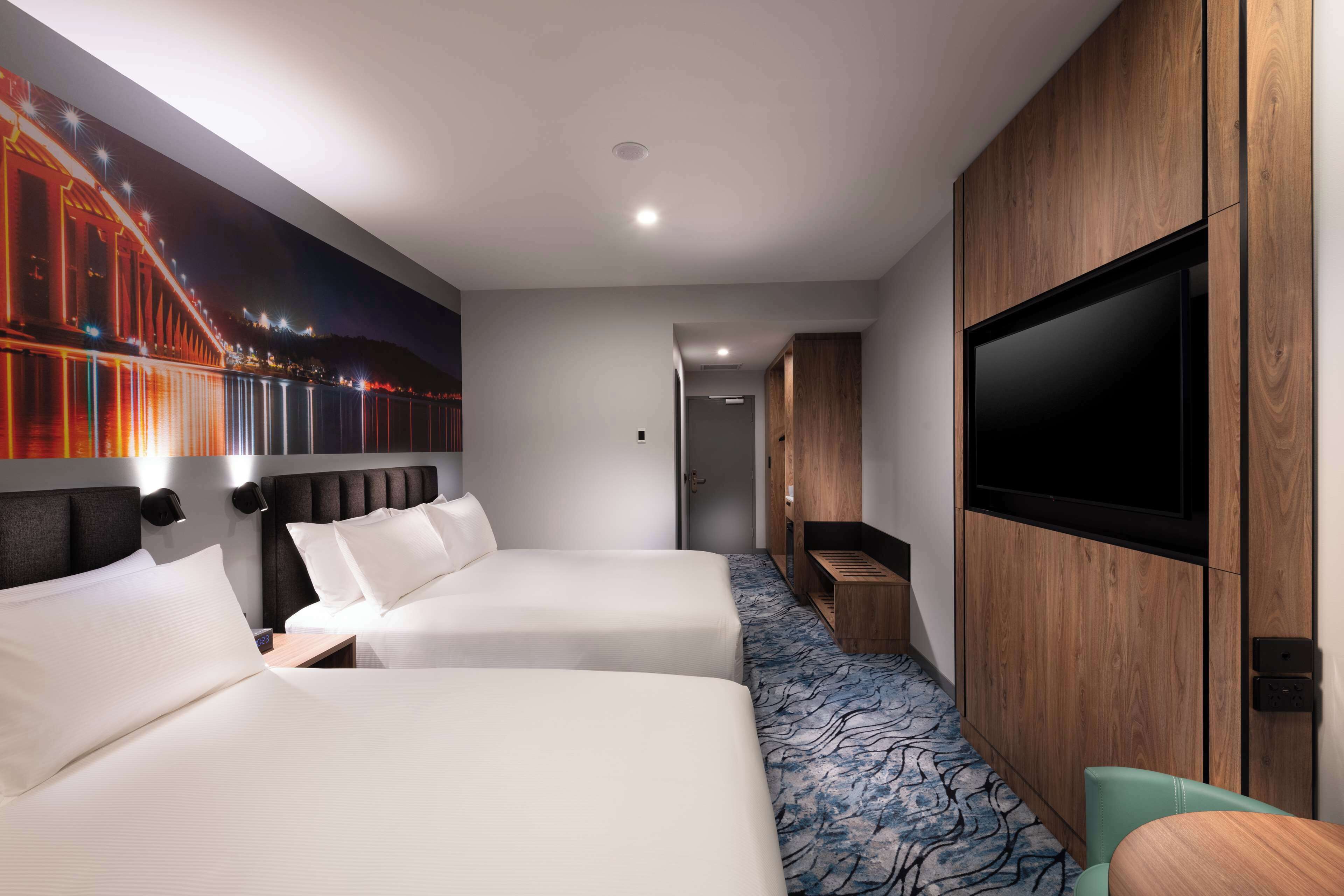 A hotel room with two beds, a TV, a wooden cabinet, and a mural of a bridge.