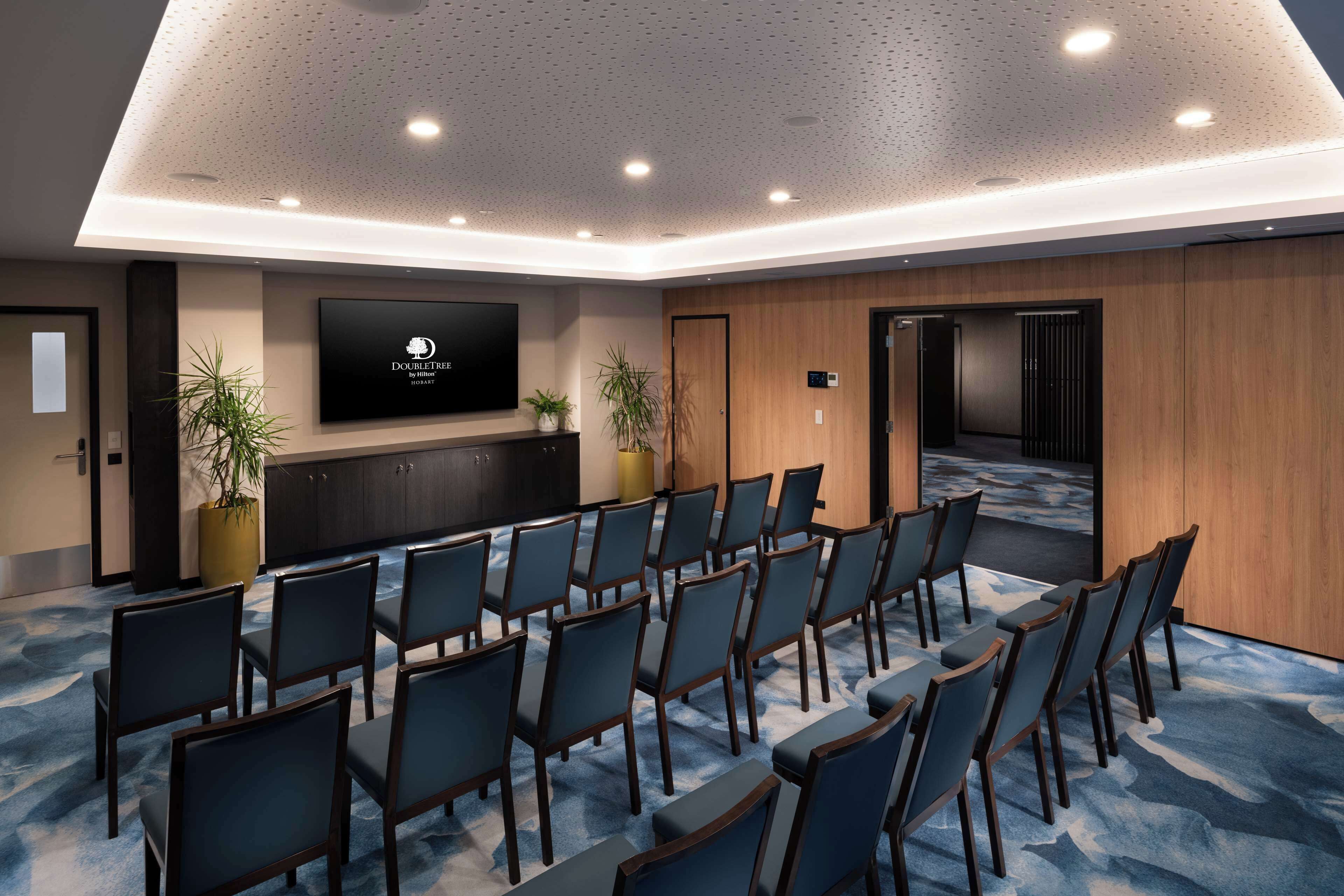A conference room with rows of chairs, a large screen, and wooden paneling.