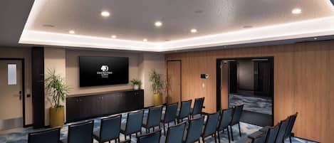 A conference room with rows of chairs, a large screen, and wooden paneling.
