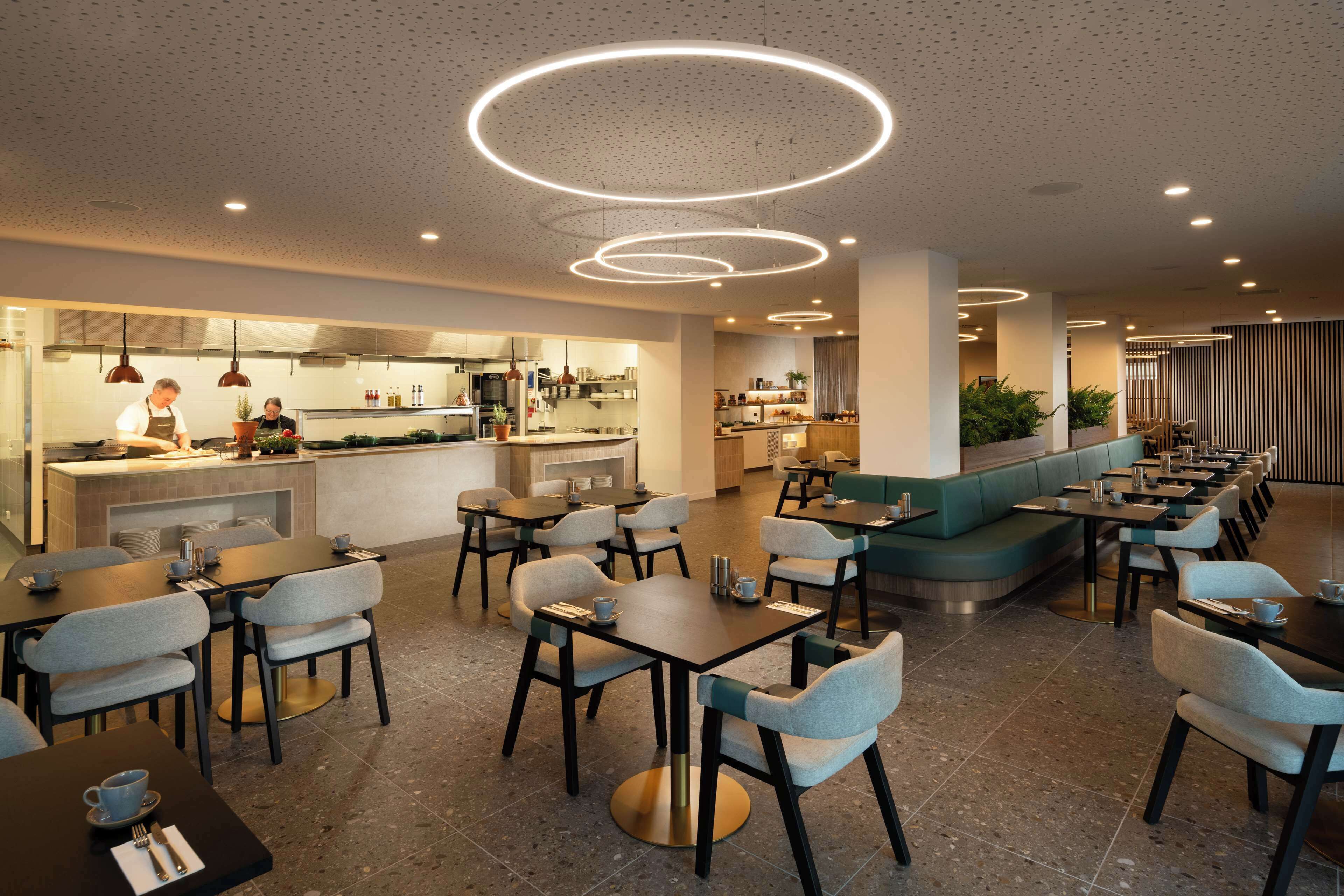 A modern restaurant with a long counter, multiple seating areas, and a bar.
