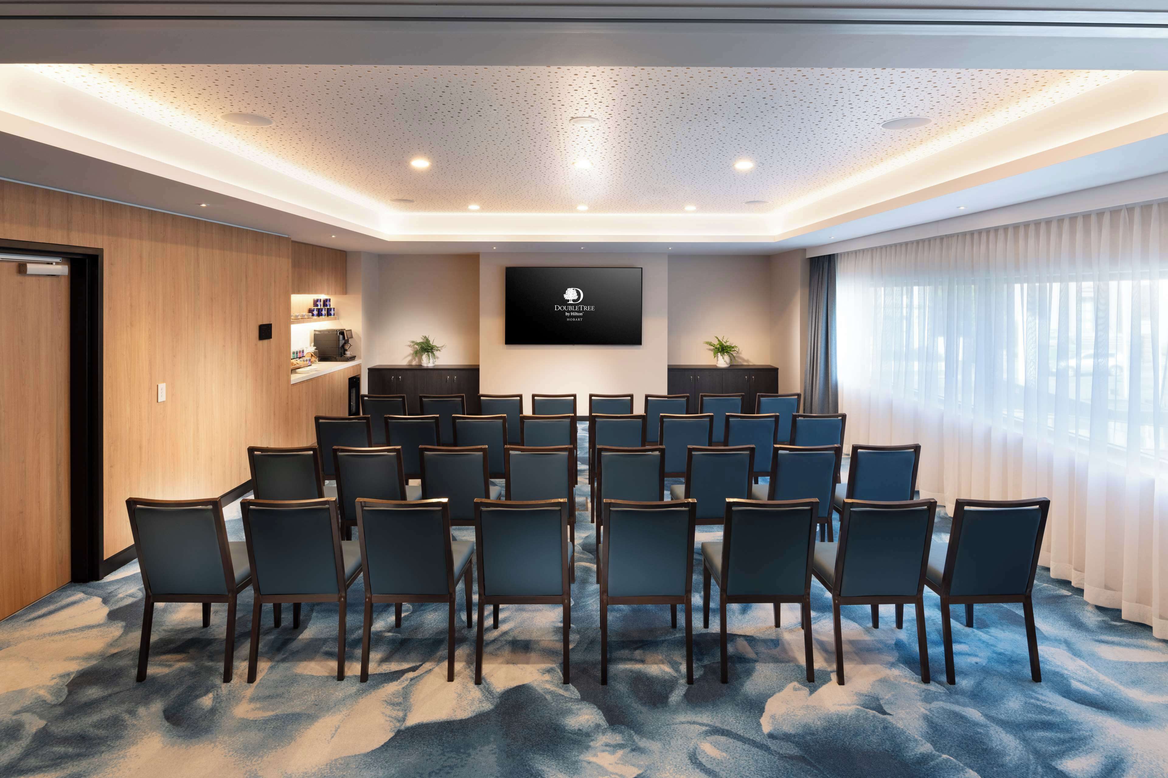 A conference room with a large screen, multiple chairs, and a carpeted floor.