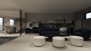 Een moderne woonkamer met een grote bank, twee witte voetenbankjes en een glazen scheidingswand.
