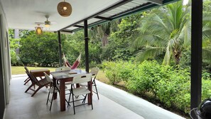 An outdoor patio with a table and chairs, surrounded by lush greenery and a view of a tropical landscape.