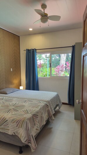A bedroom with a bed, a ceiling fan, a window with curtains, and a view of greenery outside.