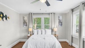 A bedroom with a bed, two bedside lamps, a ceiling fan, and a window with curtains. - Renovated Central Park Chic (Birmingham)
