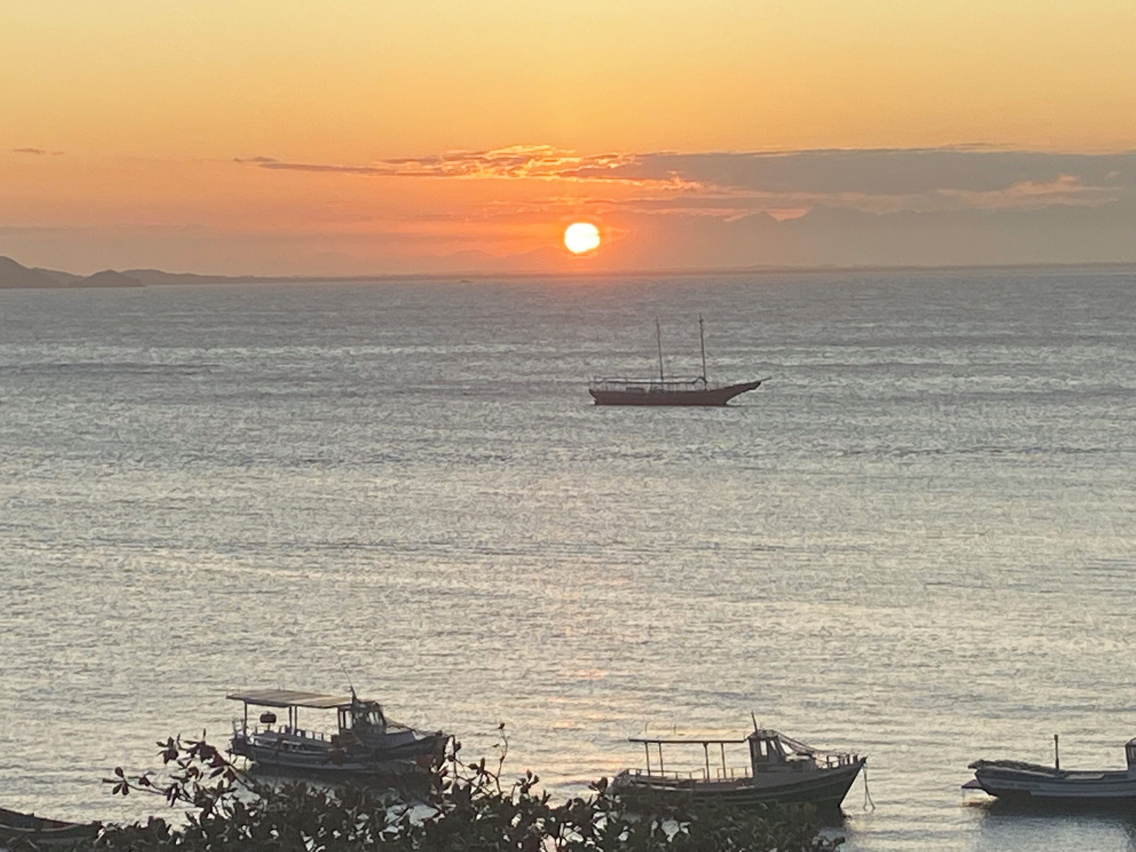 Tramonto sul mare calmo, con barche ancorate vicino alla costa.