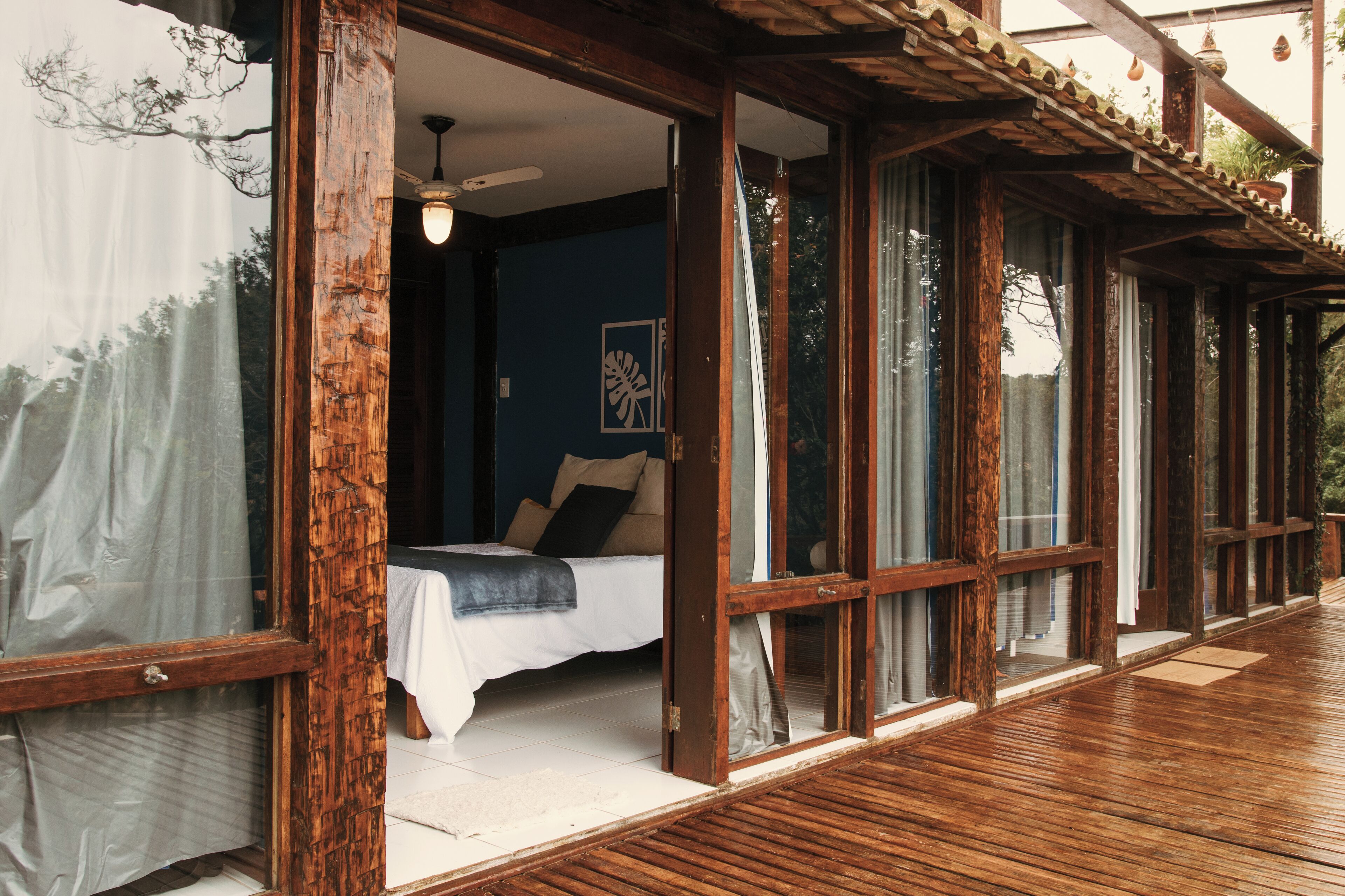 Quarto com cama, piso de madeira e janelas amplas.