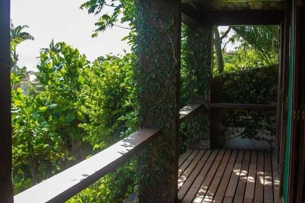 A wooden deck with a railing, surrounded by lush greenery and a stone wall.