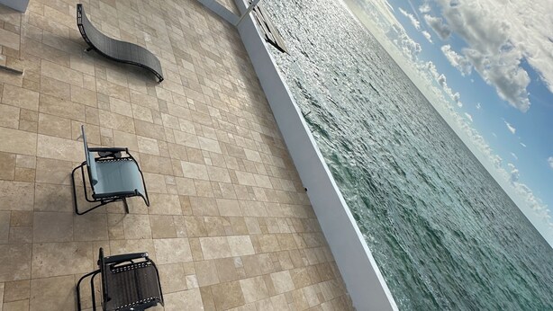 Een zonnig buitengebied met betegelde vloer, loungestoelen en uitzicht op de oceaan.