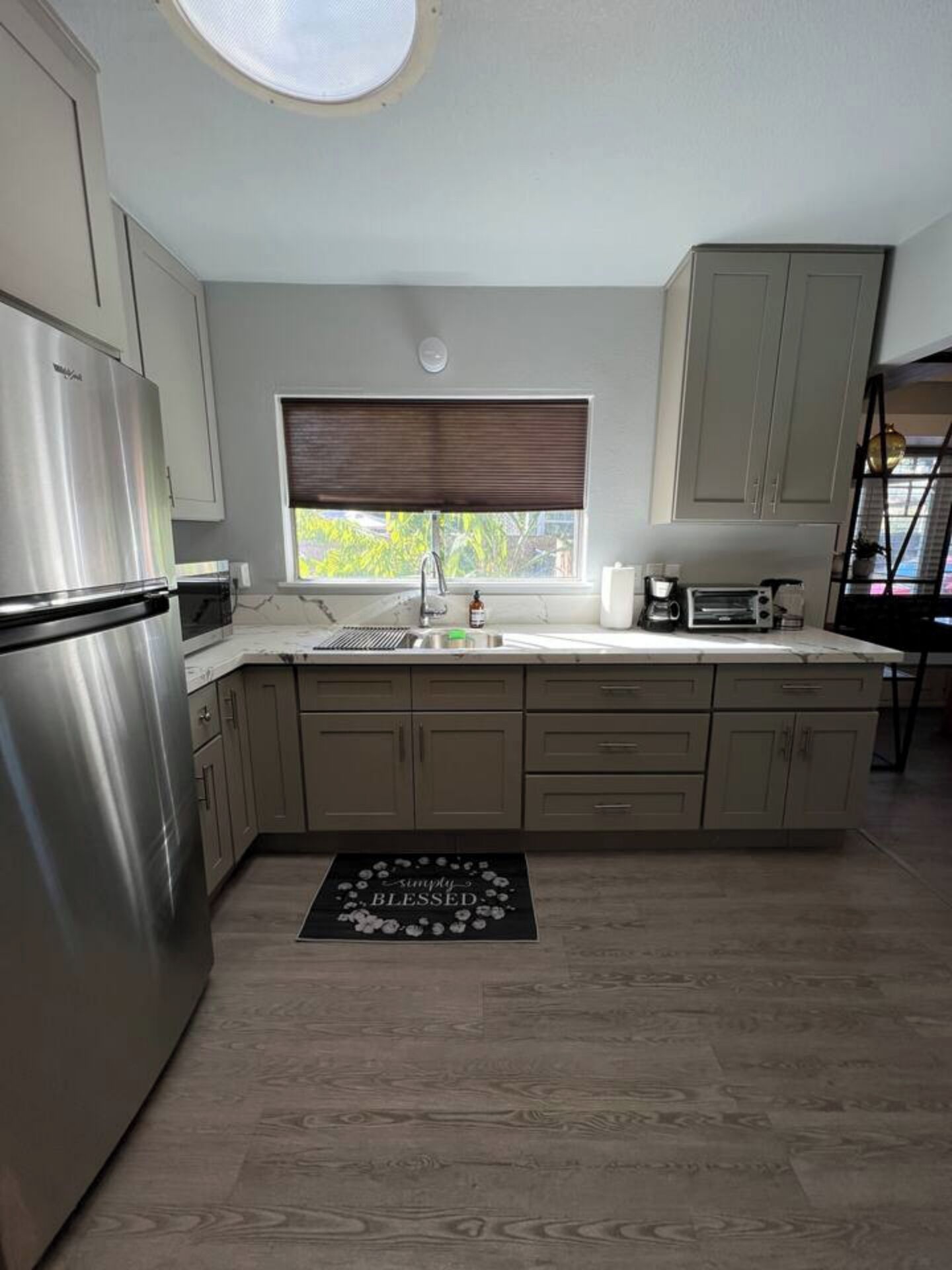 A modern kitchen with a stainless steel refrigerator, a window with blinds, a built-in oven, and a countertop with a toaster.