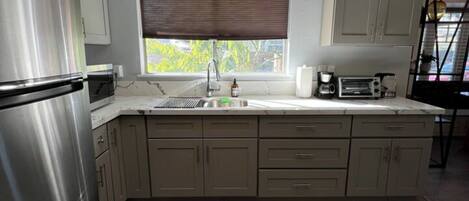 A modern kitchen with a stainless steel refrigerator, a window with blinds, a built-in oven, and a countertop with a toaster.