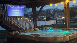 Een hottub onder een houten pergola, met een televisiescherm waarop een taalselectiemenu wordt weergegeven.