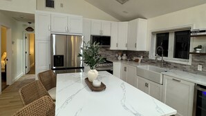 Een moderne keuken met witte kasten, een marmeren eiland, roestvrijstalen apparatuur en een groot raam.