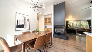 Un comedor moderno con una mesa y sillas de madera, una araña y una chimenea al fondo.