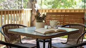 Una mesa redonda de vidrio con un borde tejido, acompañada de sillas de mimbre. Sobre la mesa, un libro, un par de gafas y una suculenta en maceta.
