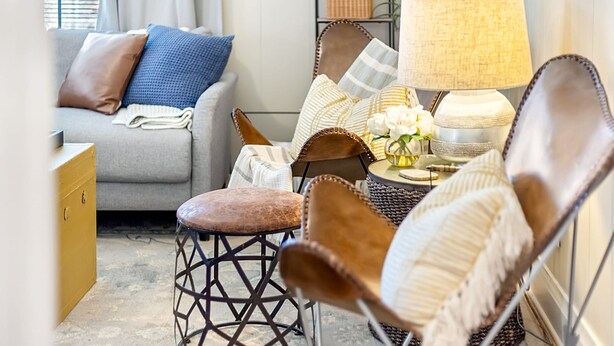 Een gezellige woonkamer met een grijze bank, een fauteuil van bruin leer en een bijzettafeltje met een lamp en decoratieve objecten.