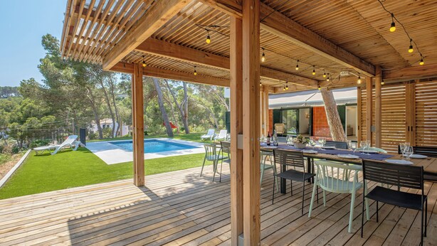 A wooden deck with a pool, outdoor seating, and a pergola with string lights.