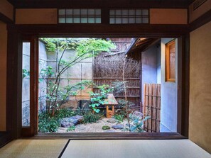 A traditional Japanese room with tatami flooring, a shoji screen, and a small garden with rocks and plants.