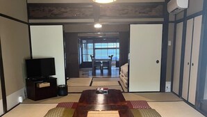 A traditional Japanese-style room with tatami flooring, a low wooden table, and a television on the left.