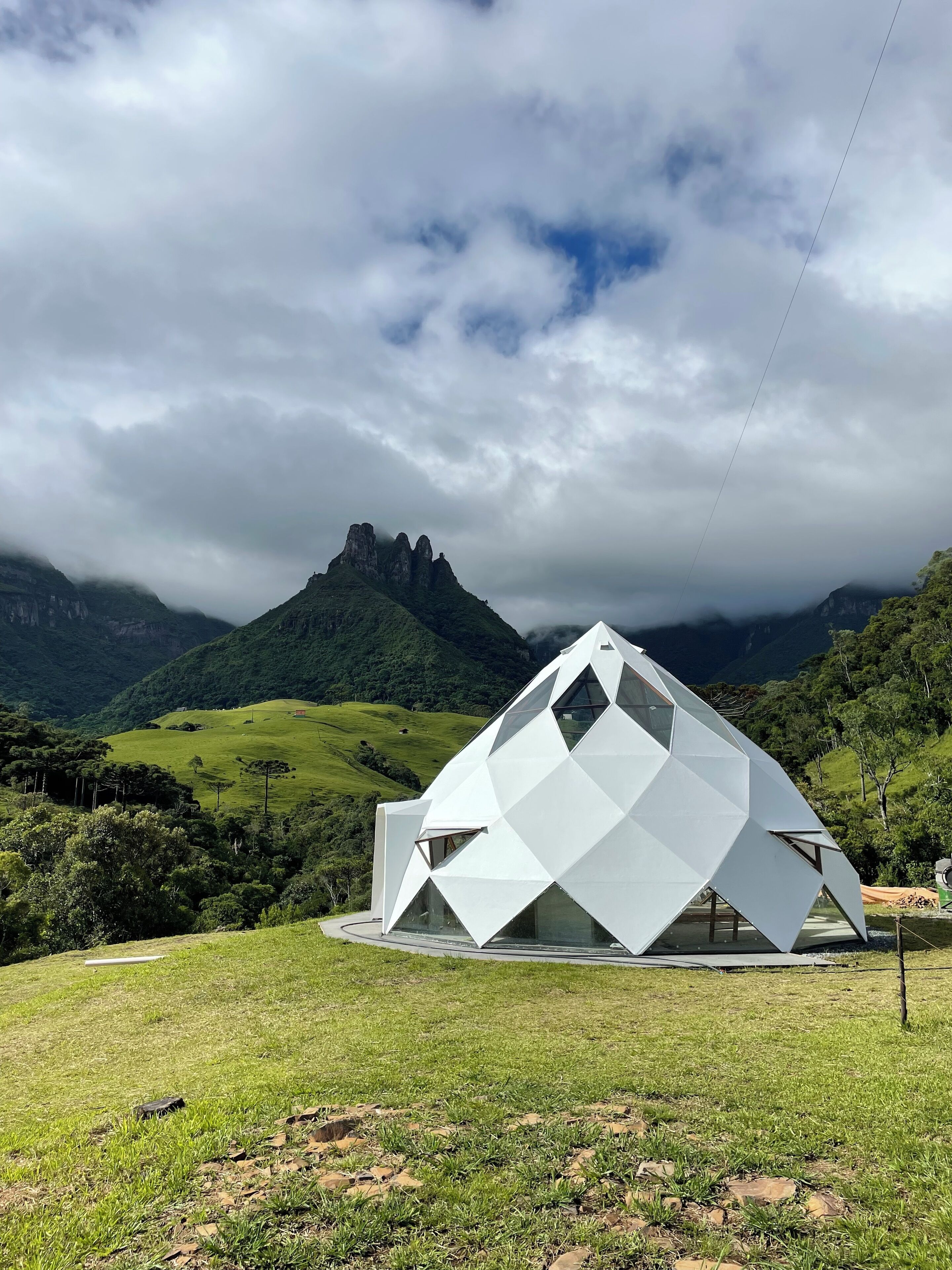 A modern, white, geometric building in a lush, green landscape with a mountain in the background.