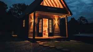 Une cabane en bois avec un toit triangulaire, une véranda et un intérieur éclairé.