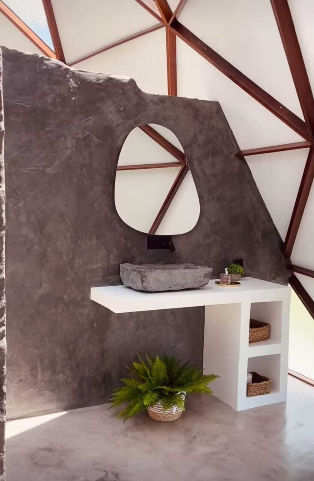 Un baño moderno con un lavabo de piedra, un espejo y una pequeña repisa con una planta.