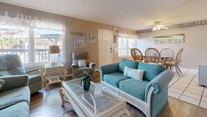 A living room with a teal sofa, two armchairs, a coffee table, and a dining area with wicker chairs. - Beach Access Across the Street, Shared Heated Pool (Corpus Christi)