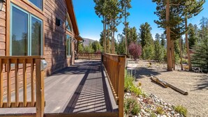 A wooden cabin with a deck, surrounded by tall pine trees and a clear sky.