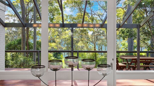 A covered outdoor area with a view of trees and a wooden deck with a table and chairs. - Home Sweet Holiday in Lilli Pilli (Lilli Pilli)