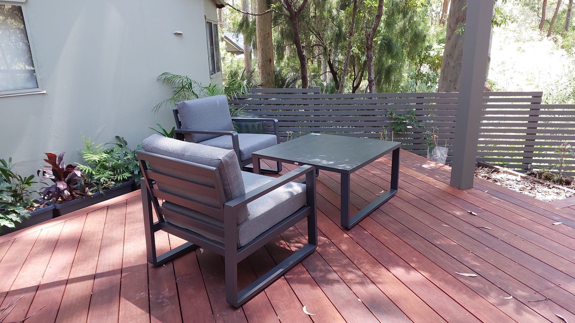 Eine Terrasse im Freien mit Holzboden, einem Metalltisch und zwei grauen Sitzgelegenheiten.