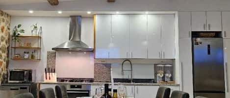 A modern kitchen with white cabinets, a stainless steel range hood, and a dining area with a long table set for six.