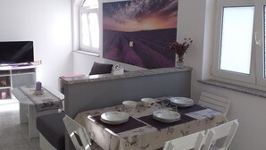 A dining area with a table set for four, a television, and a large window with a view of a field. - Apartments Lavanda & More - One Bedroom Apartment with Shared Terrace (Rab)
