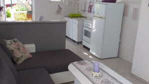 A modern kitchen with white cabinets, a stove, and a refrigerator. There is a dining area with a bench and a table. - Apartments Lavanda & More - One Bedroom Apartment with Shared Terrace (Rab)