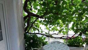 An outdoor patio with a round table and chairs, surrounded by potted plants and a view of the sea. - Apartments Lavanda & More - One Bedroom Apartment with Shared Terrace (Rab)