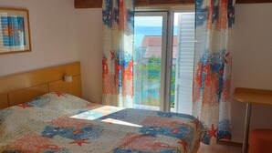 Ein Schlafzimmer mit Bett, Holz-Kopfteil, Fenster mit Vorhängen und Meerblick.