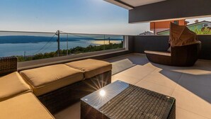 Ein moderner Balkon mit Meerblick, eine Sitzecke mit Sofa, Sessel und kleinem Tisch.