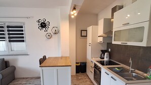 A compact kitchen with white cabinets, a wooden dining table, and a built-in microwave. - Belisima Delux - One Bedroom Apartment With Sea View (Rab)